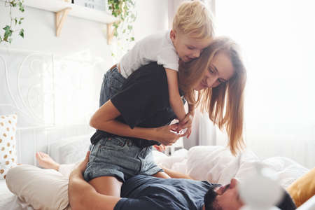 Young married couple with their young son have leisure together in bedroom at daytime.の写真素材