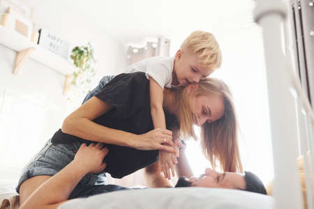 Young married couple with their young son lying down on bed and have fun together in bedroom at daytime.の写真素材