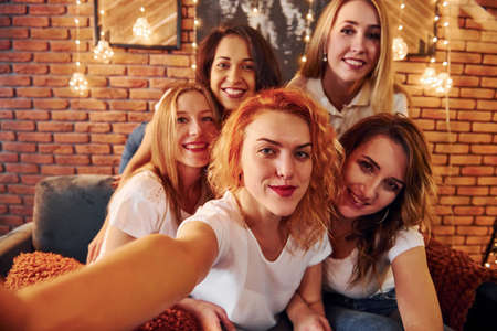 Cheerful women taking selfie and celebrating New Year holidays indoors of christmas decorated room.の写真素材