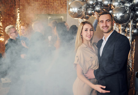 Elegant young couple standing together against their friends in christmas decorated room and...