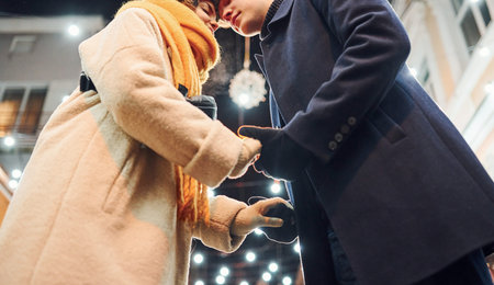 Close up view of young couple in warm clothes that is on christmas decorated street together.