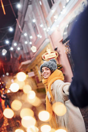 Happy young couple in warm clothes is on christmas decorated street together.の写真素材