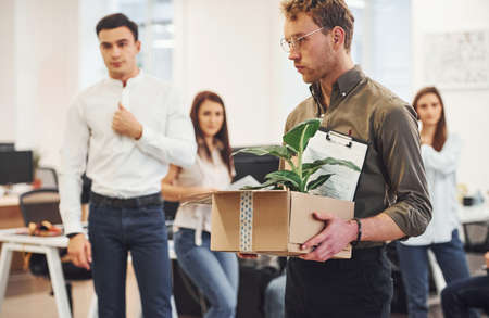 Man in glasses with box is in front of business people that working together in the modern office.の写真素材
