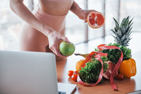 Young girl with slim body type is indoors in sportive wear near table with heatlhy food.