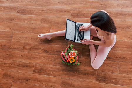 Sportive woman sitting on the table with laptop and healthy food.
