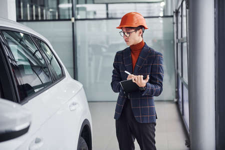 Worker in protective helmet and with notepad looking at modern car.の写真素材