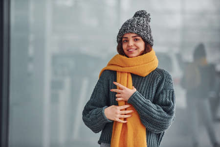 Beautiful cheerful girl in yellow scarf and in warm clothes standing indoors against background with reflections.の写真素材