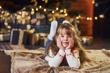Little girl lying down on the ground in the christmas decorated room.の写真素材