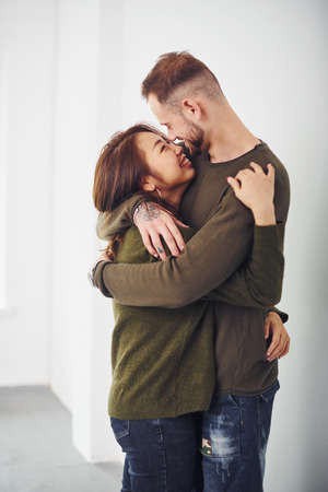 Happy multi ethnic couple in casual clothes embracing each other indoors in the studio. Caucasian guy with asian girlfriend.の写真素材