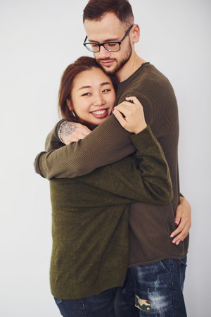 Happy multi ethnic couple in casual clothes embracing each other indoors in the studio. Caucasian...