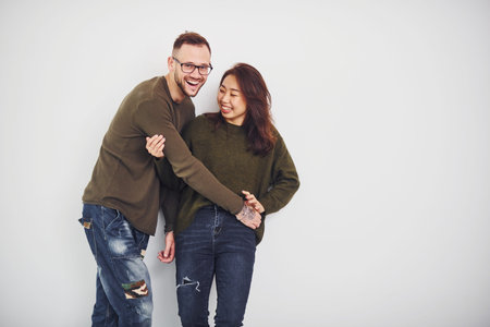 Happy multi ethnic couple in casual clothes is together indoors in the studio. Caucasian guy with...