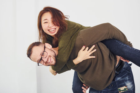 Happy multi ethnic couple in casual clothes have fun together indoors in the studio. Caucasian guy...