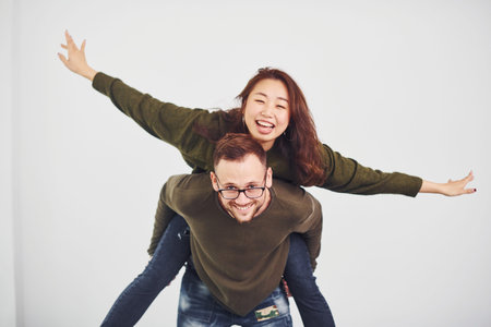 Happy multi ethnic couple in casual clothes have fun together indoors in the studio. Caucasian guy with asian girlfriend.の写真素材