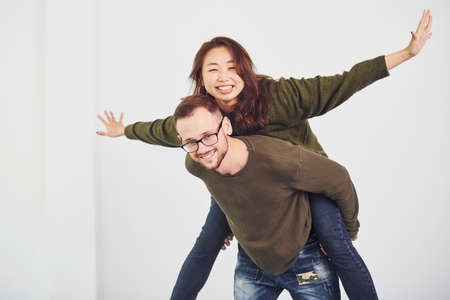 Happy multi ethnic couple in casual clothes have fun together indoors in the studio. Caucasian guy with asian girlfriend.の写真素材