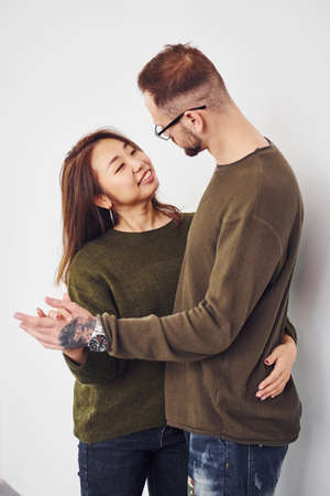 Happy multi ethnic couple in casual clothes is together indoors in the studio. Caucasian guy with asian girlfriend.の写真素材