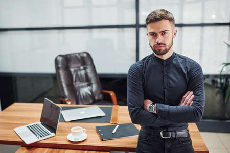Modern businessman standing indoors in office with his arms crossed.の写真素材