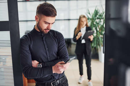 Modern businessman standing indoors in office. His female colleague behind.の写真素材
