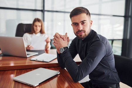 Guy sitting with documents. Woman and man in formal clothes working together indoors in the office...