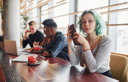 Alternative girl with green hair is sitting against group of multi ethnic people that working together by the table indoors.の写真素材