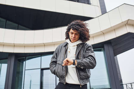Handsome young man with curly black hair posing for the camera on the street against building.の写真素材