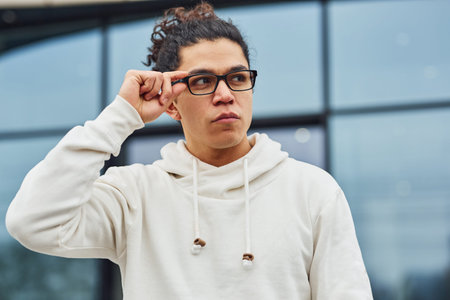 Handsome young man with curly black hair is on the street against building.