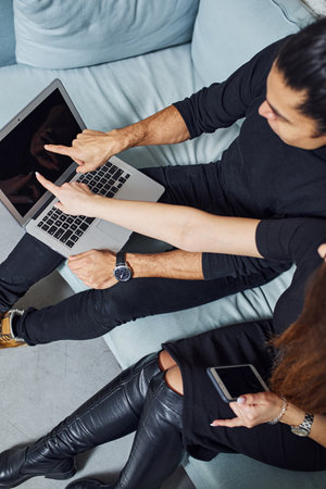 Man with curly hair and woman that in black clothes sitting with laptop indoors have a work.の写真素材