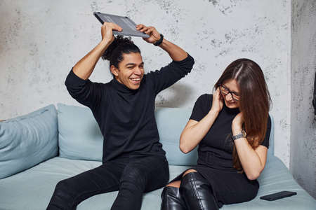 Man with curly hair and woman that in black clothes sitting with laptop indoors.の写真素材