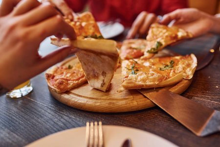 Close up view of people that taking and eating pizza indoors together.の写真素材