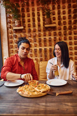 Multi ethnic young couple sitting indoors together and eating pizza.の写真素材