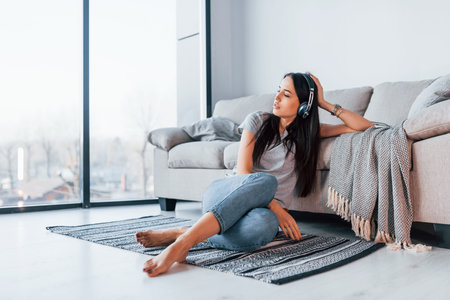 Young beautiful woman in casual clothes sitting at home alone and listening to the music in...