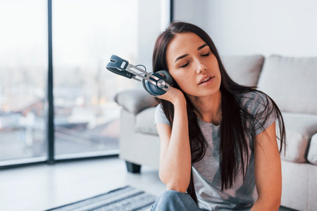 Young beautiful woman in casual clothes sitting at home alone and listening to the music in...