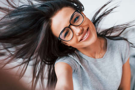 Making selfie. Young beautiful woman in casual clothes and glasses have fun at home alone.の写真素材