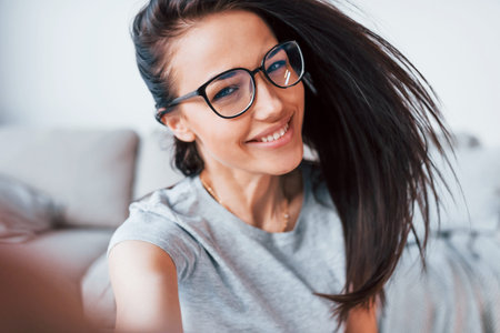 Making selfie. Young beautiful woman in casual clothes and glasses have fun at home alone.