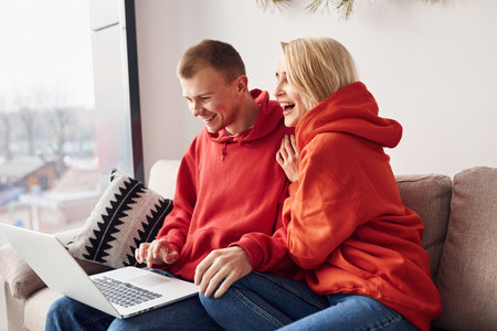 Using laptop that is on the legs. Young lovely couple together at home spending weekend and holidays...
