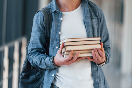 Close up view of ,ale young student in jeans clothes that is in corridor of a college with books in...
