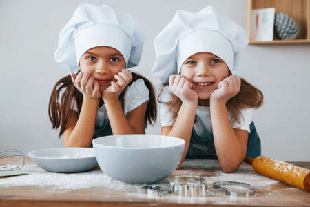 Two little girls in blue chef uniform smiling together on the kitchen.の写真素材