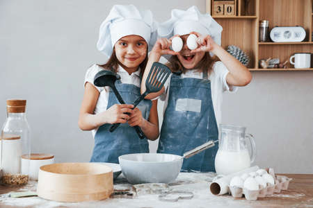 Two little girls in blue chef uniform have fun while preparing food on the kitchen.の写真素材