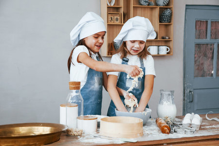 Two little girls in blue chef uniform preparing food on the kitchen.
