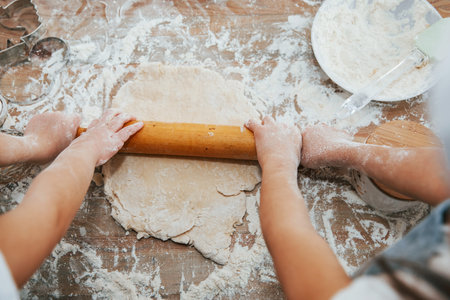 Top view of two little girls hands that preparing knead by tool on the table.