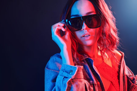Portrait of young girl in sunglasses in red and blue neon in studio.