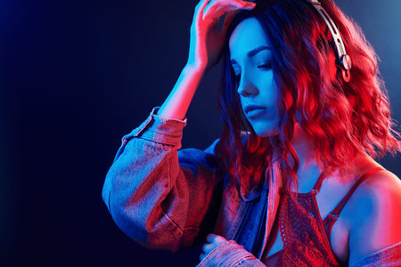 Portrait of young girl that listening to music in headphones in red and blue neon in studio.