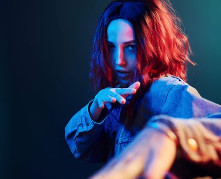Portrait of young girl with curly hair that dancing in red and blue neon in studio.