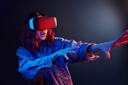 Facial expression of young girl with virtual reality glasses on head in red and blue neon in studio.