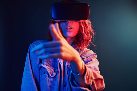 Facial expression of young girl with virtual reality glasses on head in red and blue neon in studio.