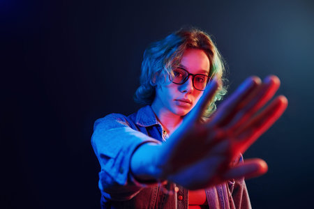 Portrait of young alternative girl in glasses with green hair in red and blue neon light in studio.