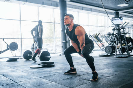 Strong young man in sportive clothes doing exercises with heavy weights in the gym.の写真素材