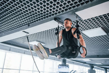 Strong young man in sportive clothes doing exercises on gymnastic rings in the gym.の写真素材