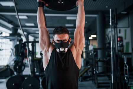 Strong young man in sportive clothes doing exercises with heavy weights in the gym.