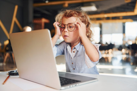 Smart child in casual clothes using laptop for education purposes or fun.