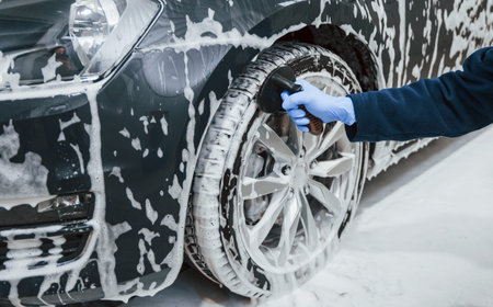 Male worker in uniform washing new modern car that covered with soap. Conception of service.